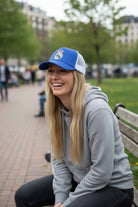 Woman wearing Fan Ink officially licensed trucker hat with embroidered soccer crest and mesh back outdoors sitting on bench